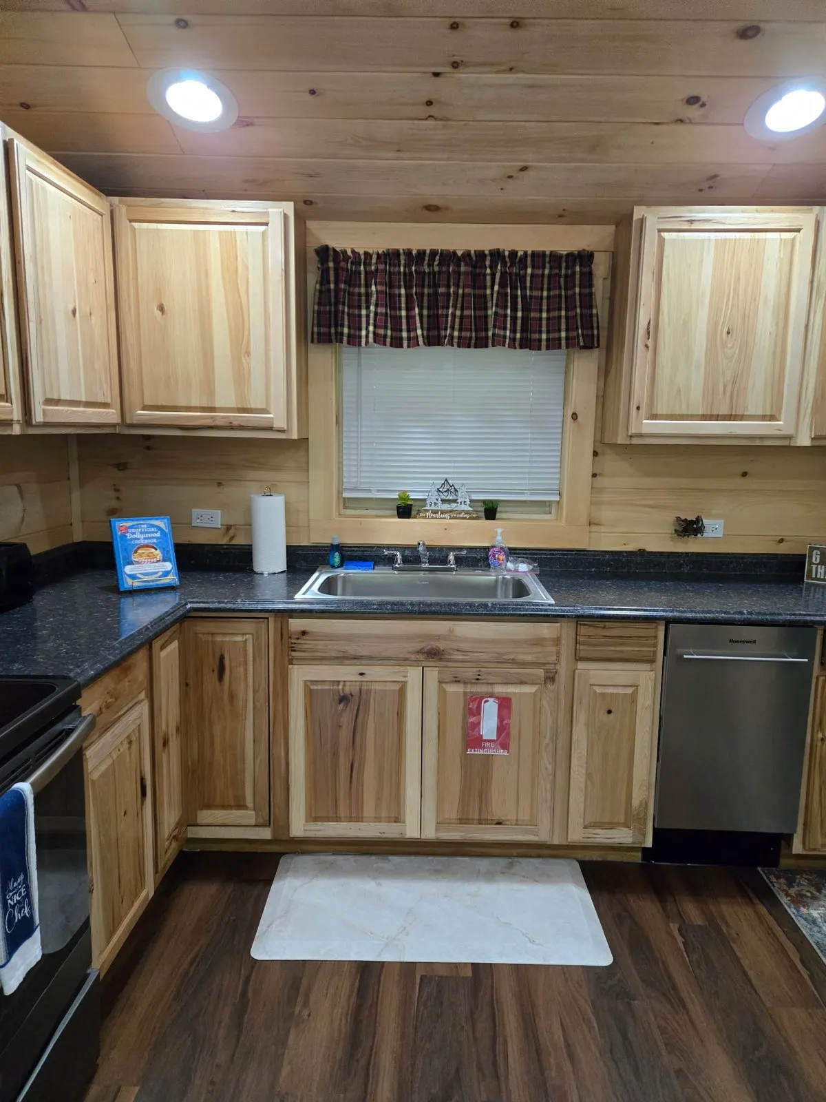 A stylish kitchen with wooden cabinets, a black granite countertop, and a window with a plaid curtain, inviting families to cook, bake, or share family recipes together. This space is perfect for baking cookies, preparing meals, or celebrating special moments.