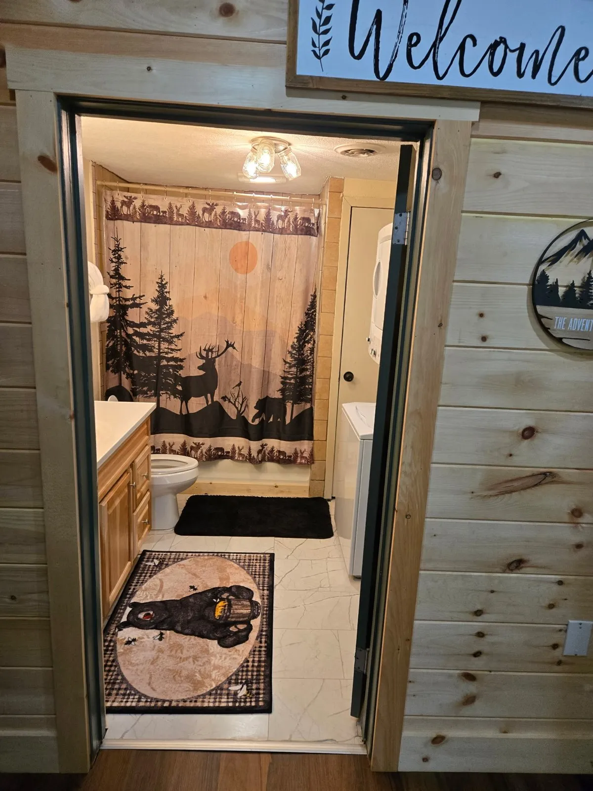 A bathroom scene with a bear-themed rug, a shower curtain adorned with nature motifs, and wooden cabinetry. The space feels rustic yet inviting, with thoughtful details and a cozy atmosphere for unwinding after a day of adventure.