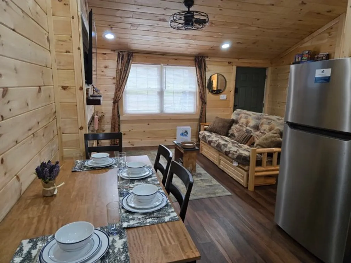 A warm, welcoming dining and living area featuring a dining table set for a meal, a comfortable sofa perfect for family gatherings, a decorative mirror, and a refrigerator. The space is arranged for casual meals, game nights, or simply relaxing together after a day of adventure.