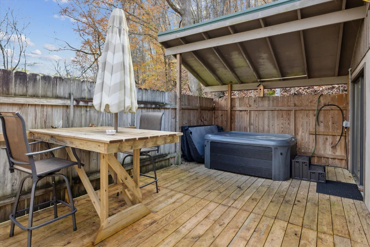 An outdoor scene featuring a private hot tub on a wooden deck, accompanied by a table and umbrella. The fenced area offers privacy, while the setup suggests intimate evenings soaking in the tub, enjoying sunset views, or dining al fresco. The natural backdrop adds to the romantic ambiance.